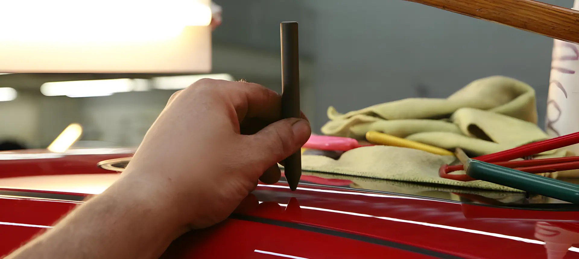 Meistras įrankiu tiesina raudono automobilio stogo įlenkimą